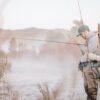 A couple fishing on a riverbank, tying the flys to the hooks for flyfishing.