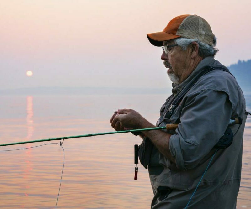 Caucasian man tying a fly on his fly fishing line while fishing for salmon and searun cutthroat