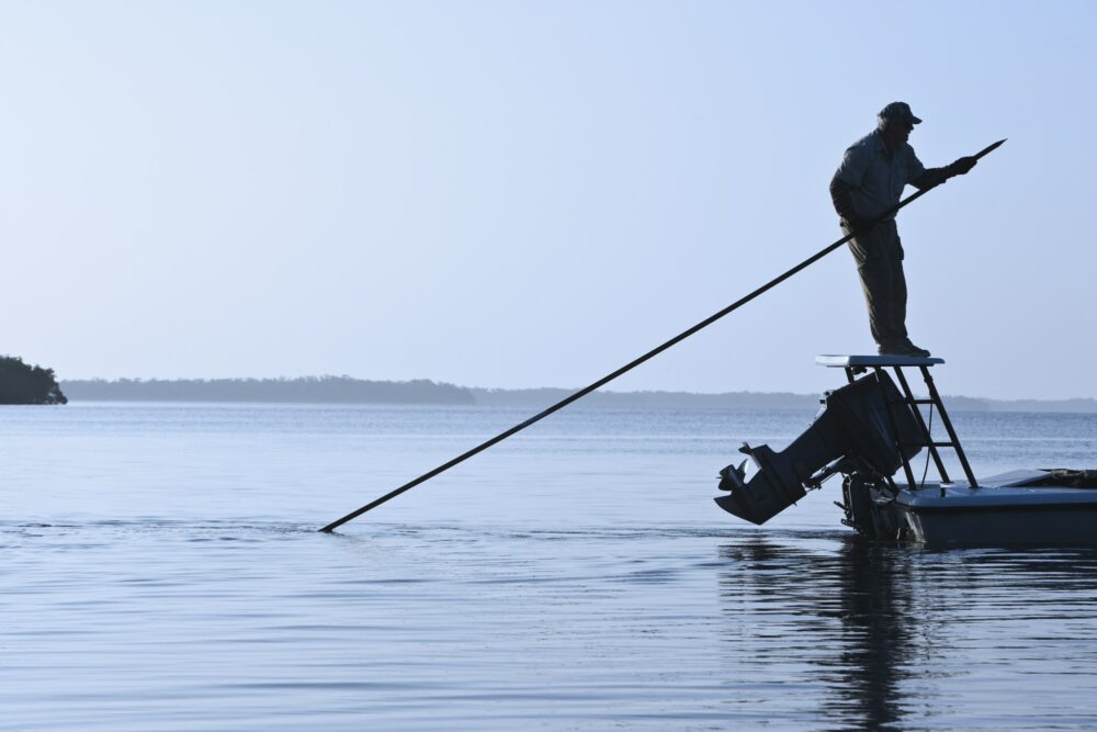 A fly fishing guide poling a flats skiff in search for tarpon and redfish along the coastline of