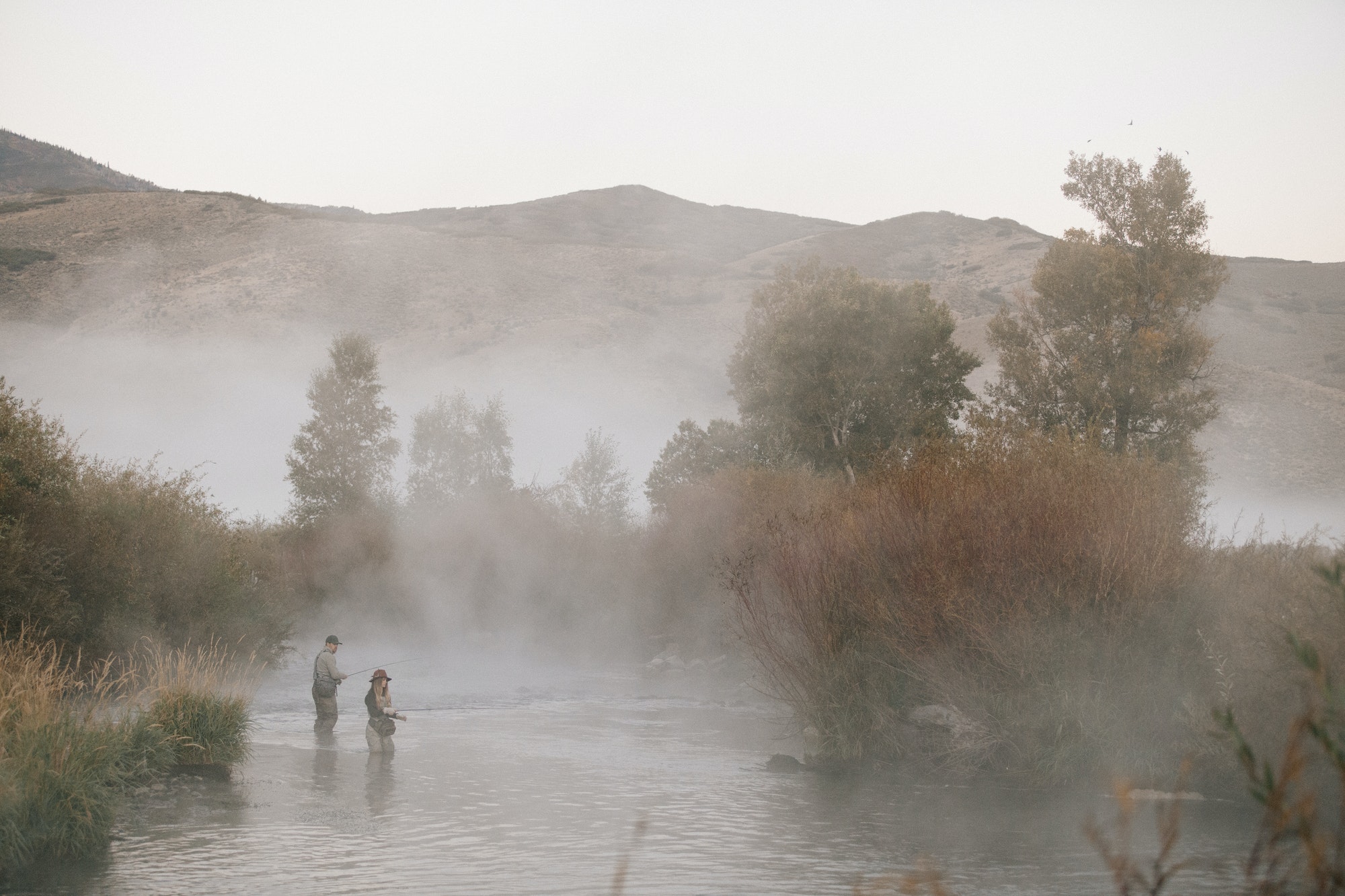 A couple, a man and woman standing in mid stream flyfishing in a river.