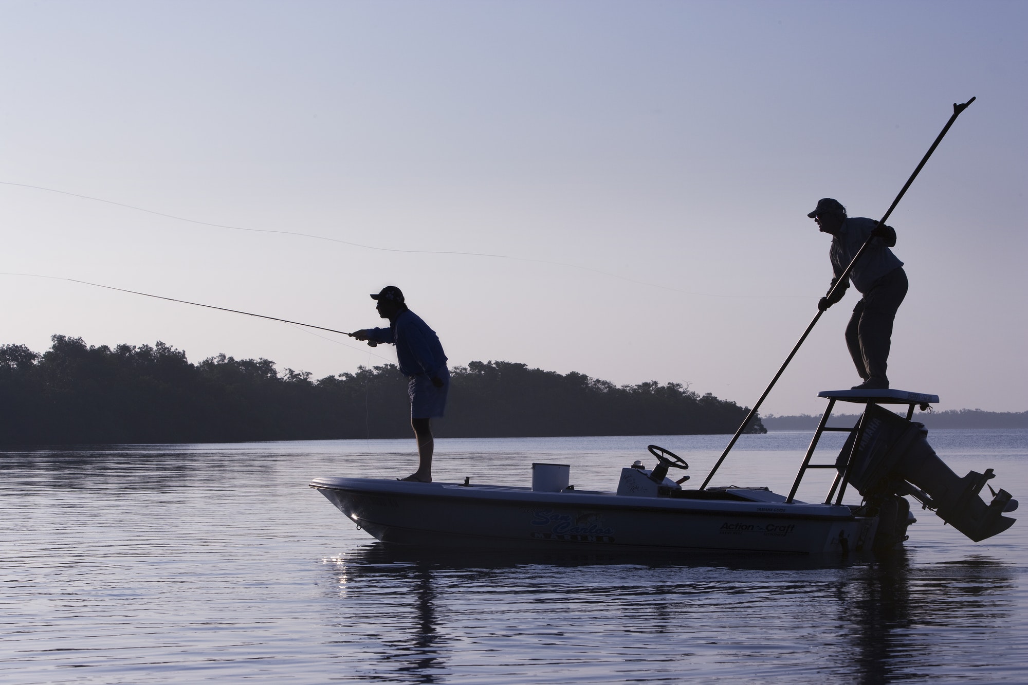 A silhouette of a fly fisherman and a guide casting for redfish from a flats boat poling skiff in