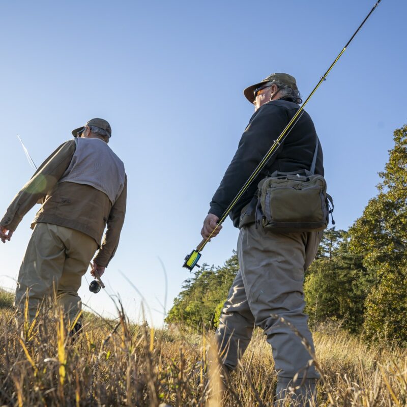 A view looking up at two fly fisherman walking a worn trail to a salt water beach in northwest
