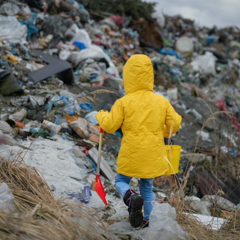 Rear view of small child walking on landfill, environmental pollution concept