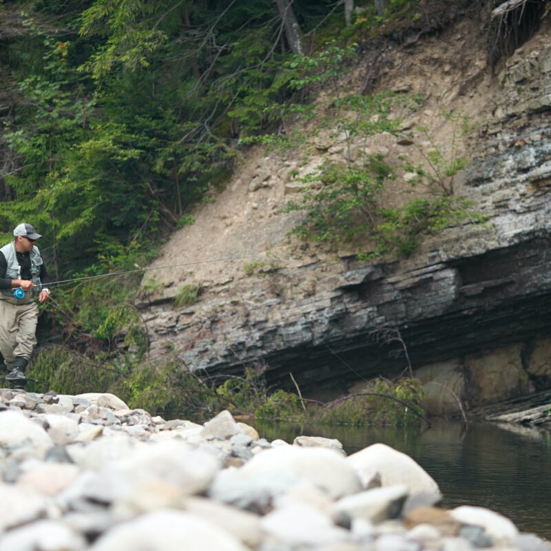 Man using rod fly fishing in rough river among mountain