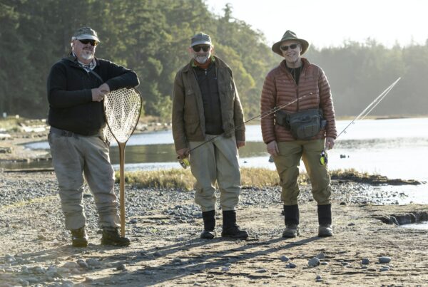 A portrait of two caucasian male fly fishermen and their fly fishing guide standing on a beach on