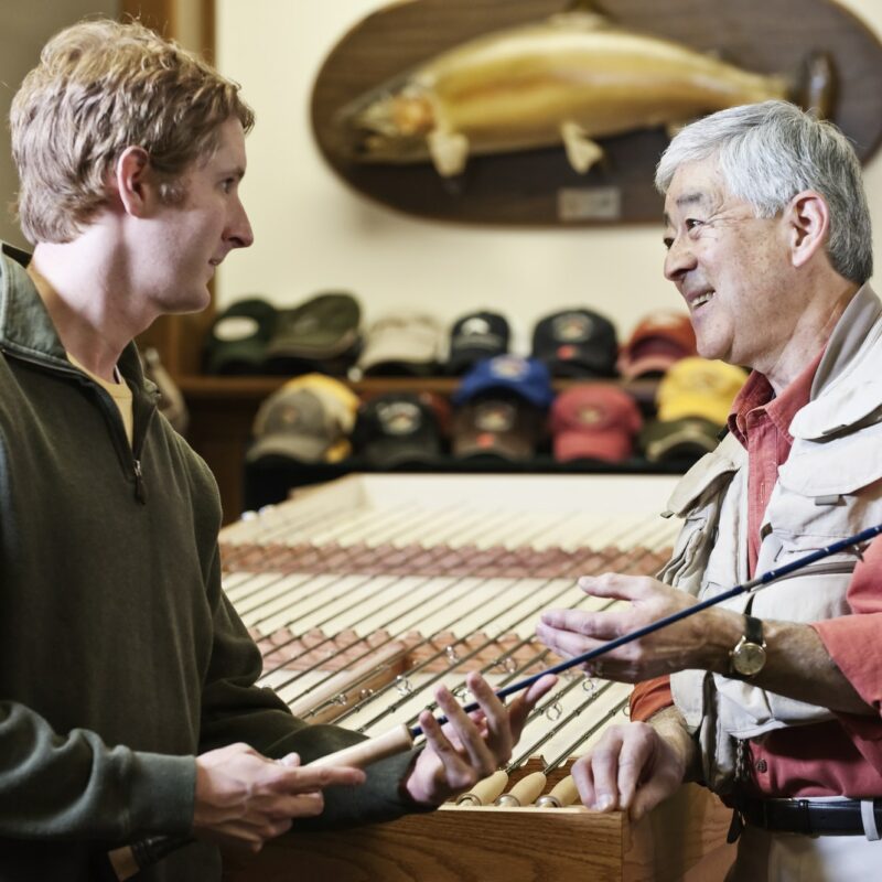 Male owner of a retail fly-fishing shop talking to a young caucasian customer sharing expertise