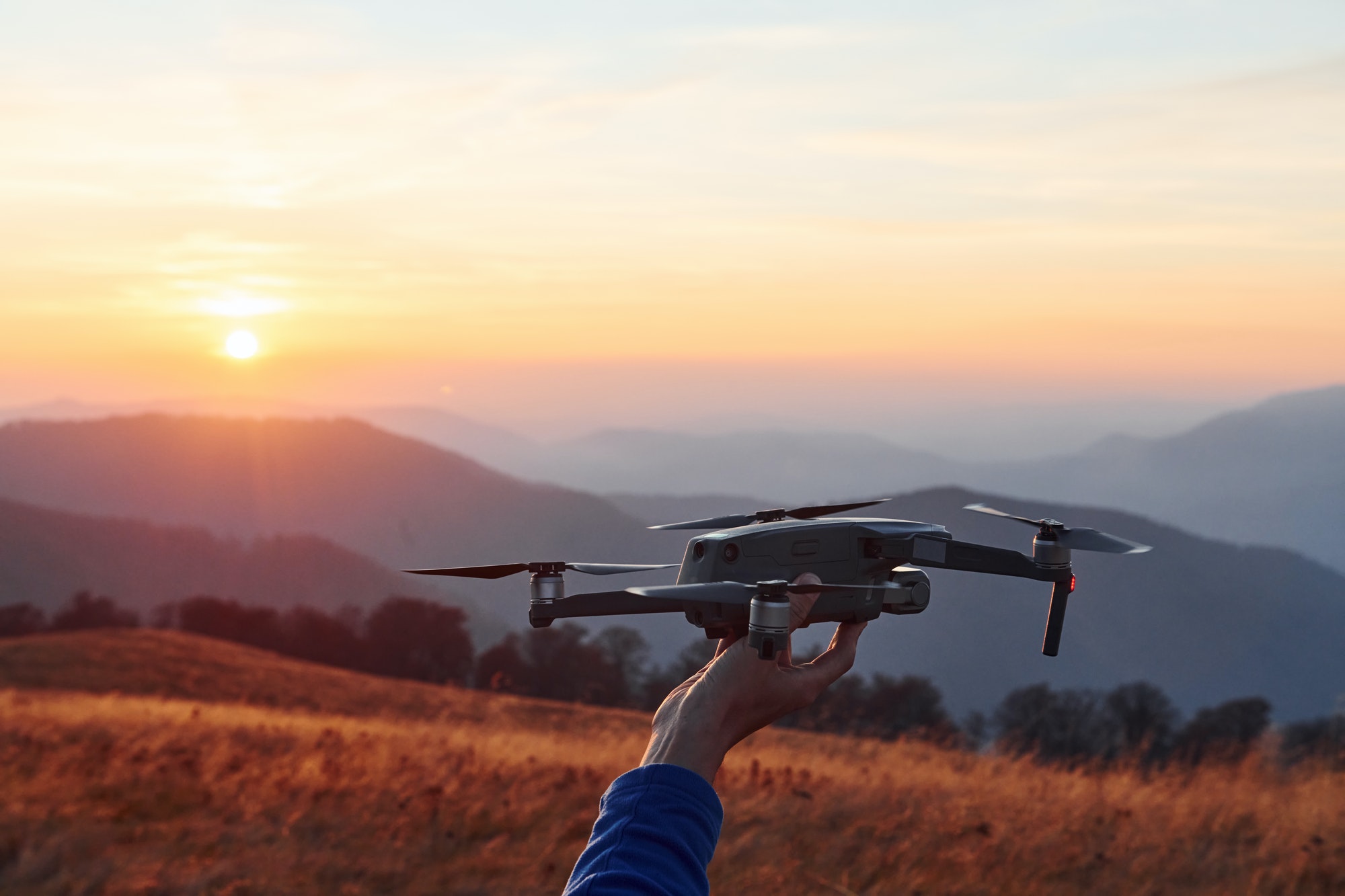 Man standing in the autumn field and holds drone in hand. Beautiful sunrise. Majestic landscape