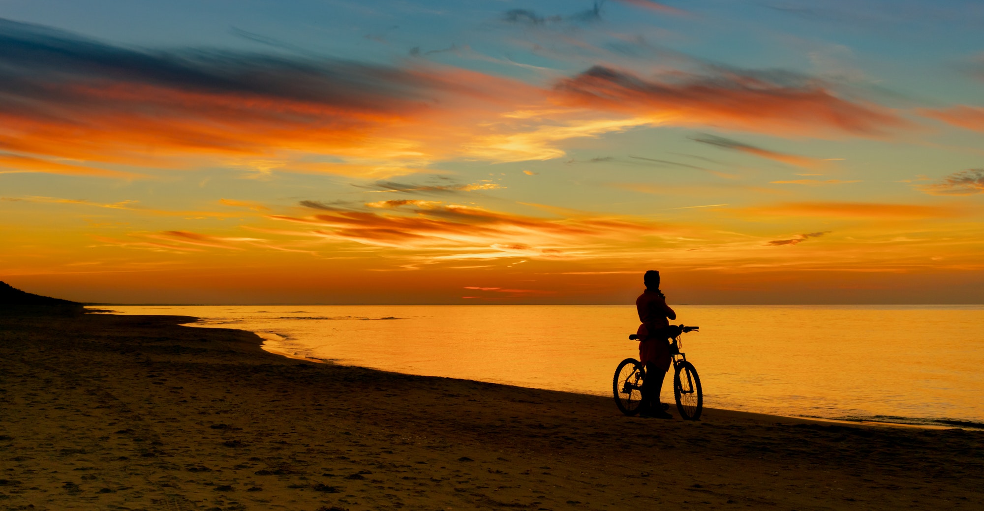 Silhouette of cyclist on beach against backdrop of sunset at sea shore