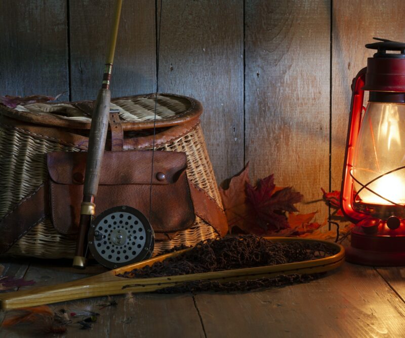 Vintage fly fishing rod creel and net with lantern on old wood background