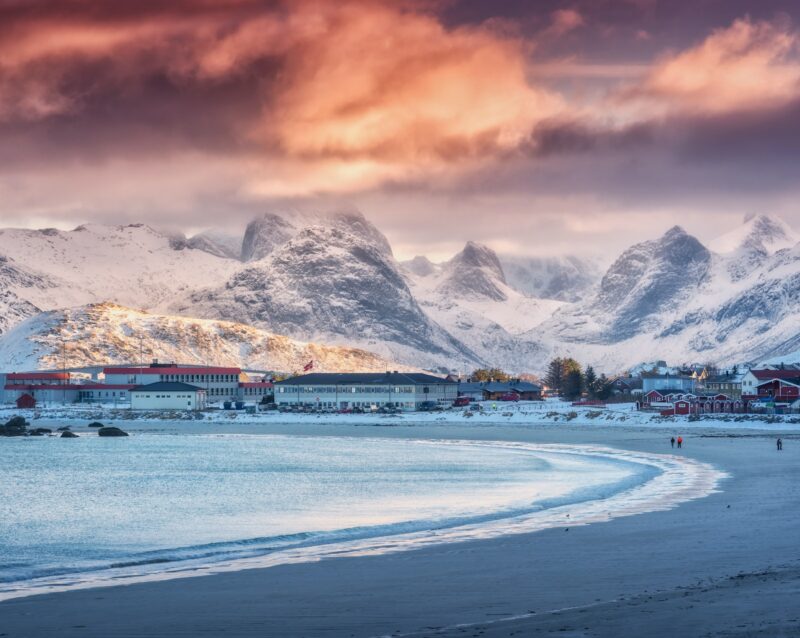 Arctic sandy beach, blue sea and snowy mountains at sunset