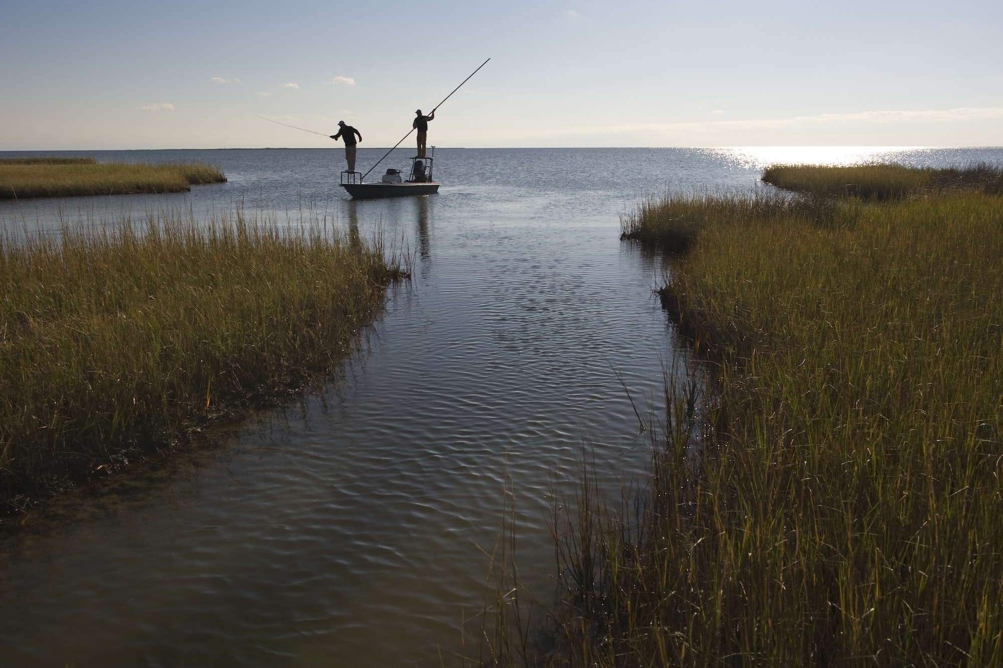 A silhouette of a fly fisheman and a guide casting for redfish from a flats boat poling skiff in