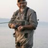 Caucasian senior male tying a fly on his fly fishing line while fishing for salmon and searun