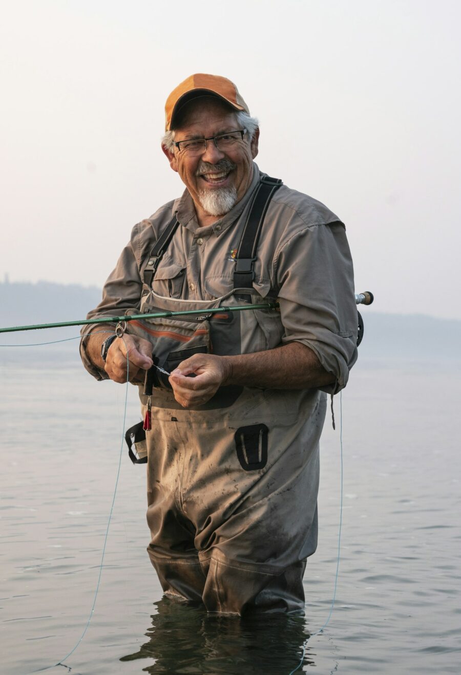 Caucasian senior male tying a fly on his fly fishing line while fishing for salmon and searun